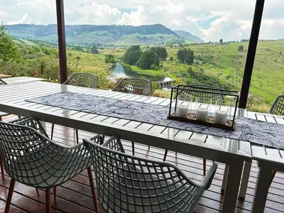 a table with chairs on a wooden deck with a view at Waterfall House in Dullstroom