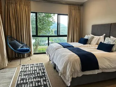 a bedroom with two beds and a chair and windows at Waterfall House in Dullstroom