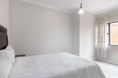 a white bedroom with a bed and a window at Lovely 2 bed @TheBlyde in Pretoria
