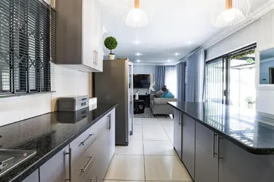 a kitchen with black counter tops and a living room at Patimo Opulent Accommodation -Pretoria Mayville,Gezina in Pretoria