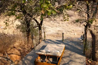 a table and chairs on a wooden walkway with trees at Villa Kudu - Exclusive and Serviced Safari Villa near Kruger Park in Hoedspruit