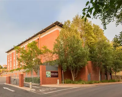 a red brick building with trees next to a street at Road Lodge Centurion in Centurion