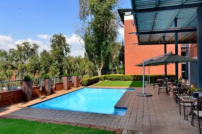 a swimming pool with tables and chairs and an umbrella at Road Lodge Centurion in Centurion