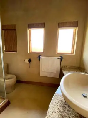 a bathroom with a sink and a toilet and windows at Reedbuck Lodge @Cyferfontein in Mabalingwe Reserve in Bela-Bela