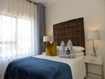 a bedroom with a bed with a blue blanket and pillows at Eirini Elegant - Ares Apartment Carlswald in Midrand