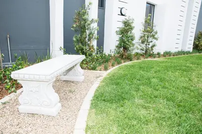 a white bench sitting in the grass in front of a house at Eirini Elegant - Ares Apartment Carlswald in Midrand
