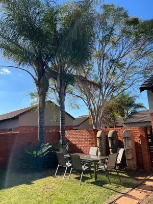 a patio with a table and chairs and palm trees at Centurion Ambient Townhouse in Centurion