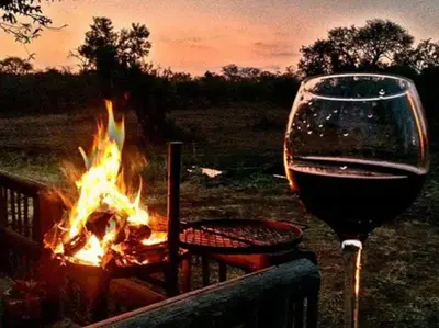 a glass of wine sitting next to a fire at Zebula Golf and Wildlife Estate - Jackals Call Pax 8 - Moi Signature Luxury villa in Mabula