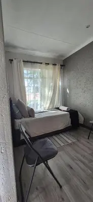 a bedroom with a bed and a chair and a window at Die Eend in Centurion