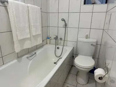 a white bathroom with a toilet and a bath tub at Busa House in White River