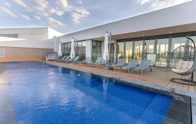 a large swimming pool with chairs and a building at Menlyn Maine Trilogy Apartment 611 in Pretoria