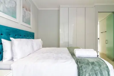 a bedroom with a large white bed with a blue headboard at #AlimamaSpaces: Jay's Cassini in Midrand