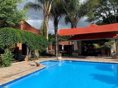 a large blue swimming pool with a red umbrella at Bougain Villa Guest House in Polokwane