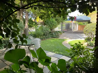 a patio with a table and a chair in a garden at Bougain Villa Guest House in Polokwane