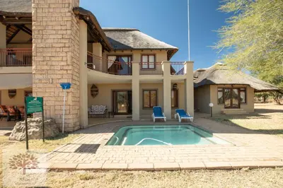 a villa with a swimming pool in front of a house at Zebula Golf and Wildlife Estate - Owl's Haven Pax 10 - Moi Signature Luxury villa in Mabula