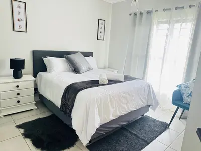 a white bedroom with a bed and a chair at The Blyde Holiday beach in Pretoria