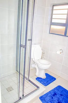 a bathroom with a toilet and a shower with blue rugs at The Blyde Holiday beach in Pretoria