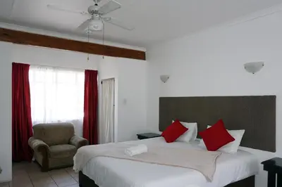 a bedroom with a bed with red pillows and a chair at Sheba Rock Guesthouse in Nelspruit