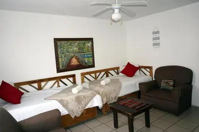a bedroom with two beds and a chair and a ceiling fan at Sheba Rock Guesthouse in Nelspruit