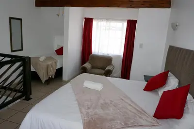 a bedroom with a bed with red pillows and a chair at Sheba Rock Guesthouse in Nelspruit