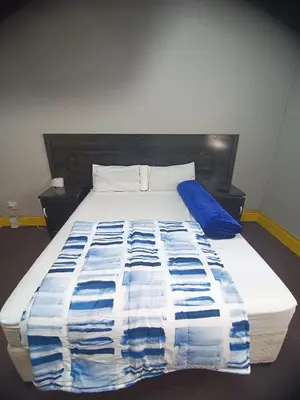 a bed with a blue and white blanket on it at Prime Guest Inn in Benoni