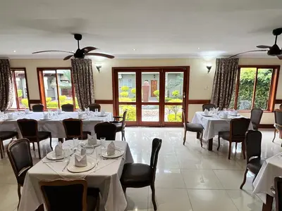 a dining room with white tables and chairs and windows at Limpopo Guest Manor in Polokwane
