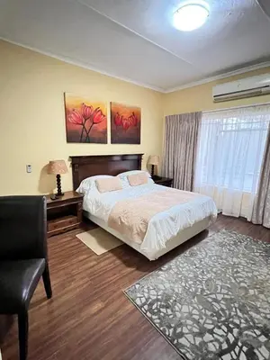 a bedroom with a bed and a chair and a window at Limpopo Guest Manor in Polokwane