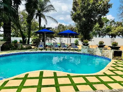 a swimming pool with blue umbrellas and chairs at C'est La Vie Boutique Hotel in Witbank
