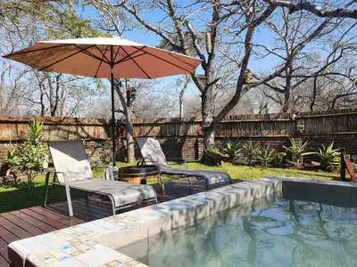 a patio with two chairs and an umbrella next to a pool at Vuurvliegie in Marloth Park