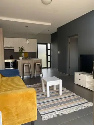 a living room with a yellow bed and a kitchen at The Blues in Pretoria