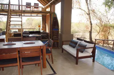 a dining room with a table and chairs and a balcony at Kruger River Holiday Home in Marloth Park