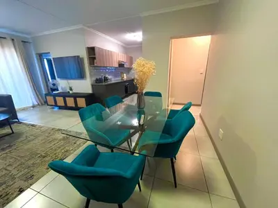 a living room with a glass table and blue chairs at Large 3 Bedroom Apartment in Midrand, Waterfall City - More space than a hotel room - Ideal for families, groups and work trips - 16 Elizabeth Place in Midrand