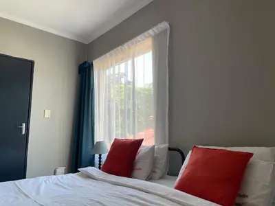 a bedroom with a bed with red pillows and a window at Smartshelter Park in Pretoria