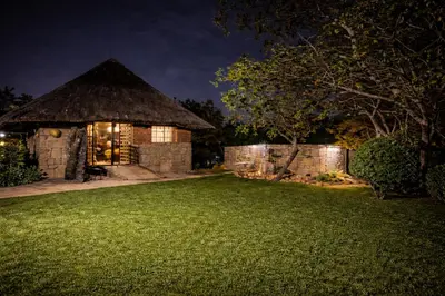 a house with a thatch roof at night at 5 Sleeper Bushcamp Chalet Hartbeespoort in Hartbeespoort