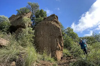 a man walking on a trail next to a large rock at 5 Sleeper Bushcamp Chalet Hartbeespoort in Hartbeespoort