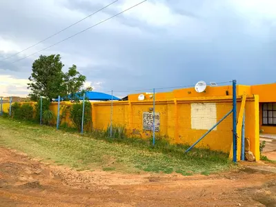 a fence next to a yellow building on a dirt road at Bobirwa Resort & Accomodation in Polokwane
