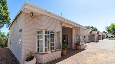 a white brick building with potted plants in front of it at Plumtree Lodge in Polokwane