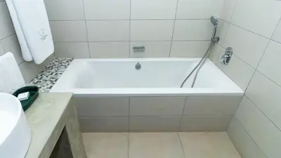 a white bath tub in a white tiled bathroom at Plumtree Lodge in Polokwane