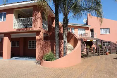 a pink building with palm trees in front of it at El Gran Chaparral Guest House in Pretoria