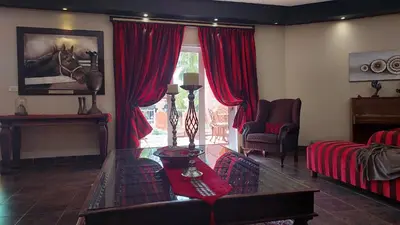 a living room with red curtains and a glass table at El Gran Chaparral Guest House in Pretoria