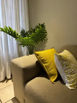 a couch with two yellow pillows and a plant at Thorntree Self Catering Apartment, Witbank in Witbank