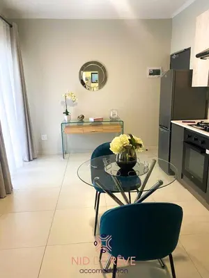 a living room with a glass table and a kitchen at Nid de Rêve Accommodation in Midrand