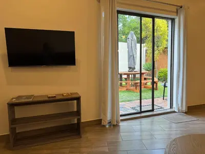 a living room with a tv and a sliding glass door at De Vlei - Private Accommodation in Garsfontein in Pretoria