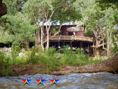 three colorful kites in the water next to a house at Blyde River Cabins in Hoedspruit