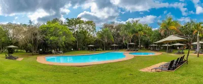 a swimming pool in a park with trees and umbrellas at Kruger Park Lodge Unit No. 516 in Hazyview