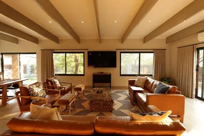 a living room with brown leather furniture and windows at Shiandi Villa in Hoedspruit