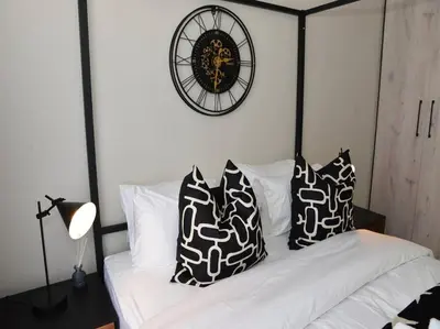 a bed with black and white pillows and a clock at ELcaro Luxury Villas-The Cave in Midrand