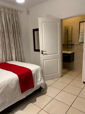 a bedroom with a bed with a red blanket and a bathroom at A Stunning Cozy Apartment in Midrand