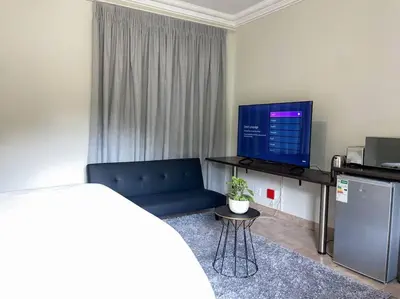 a living room with a blue couch and a flat screen tv at Bobisemo Luxury Pretoria East Apartment in Tierpoort