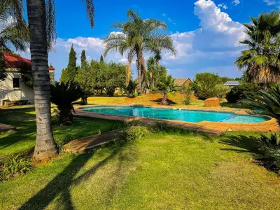 a swimming pool in a yard with palm trees at Bobisemo Luxury Pretoria East Apartment in Tierpoort